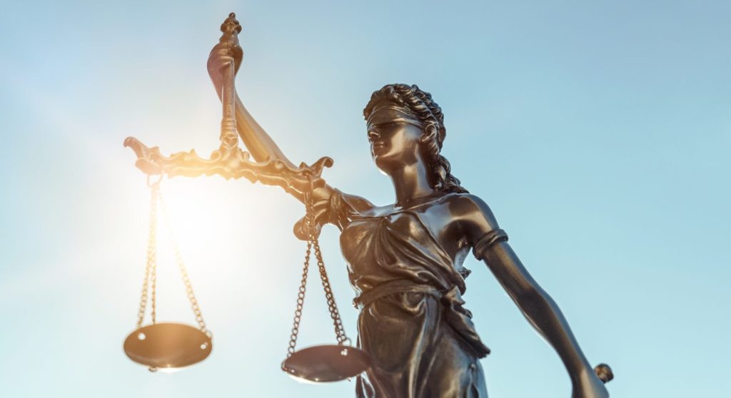 Beeld van vrouwe justitia voor blauwe, zonnige achtergrond