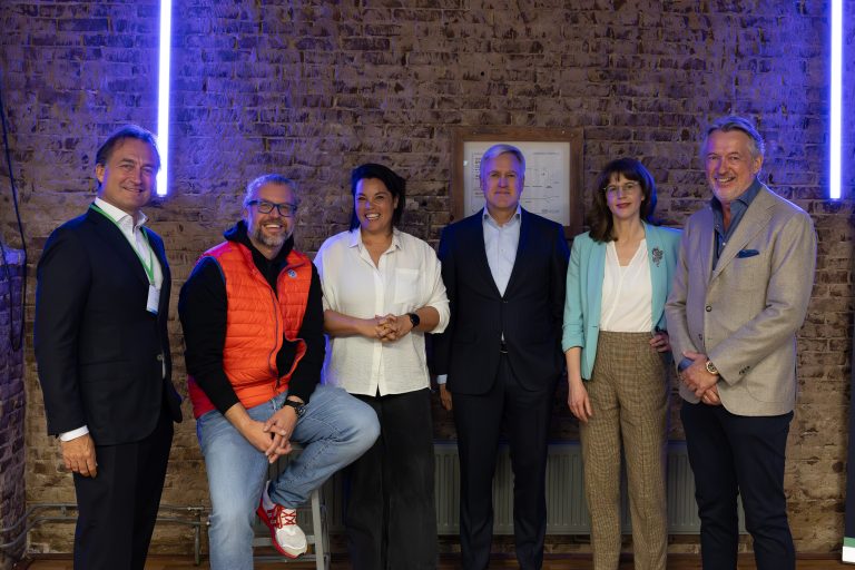 Vijf personen poseren voor een muur in een informele setting.