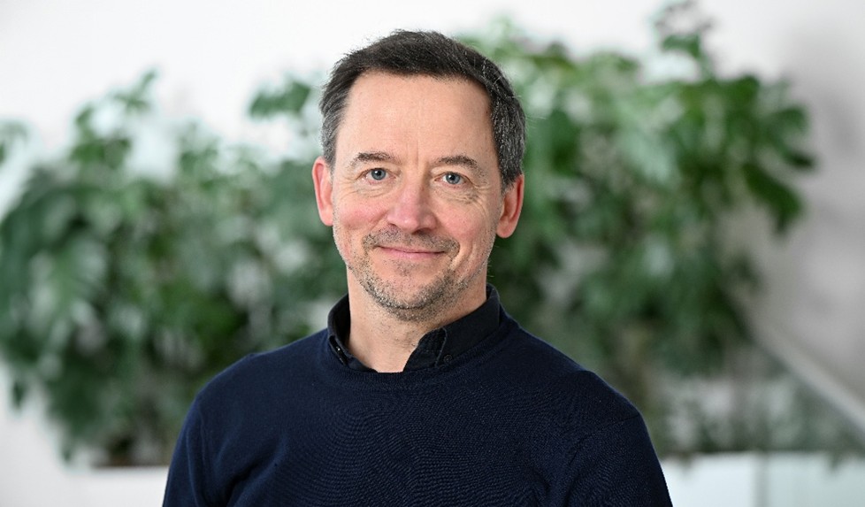 Man met kort haar en een blauwe blouse en natuurlijke achtergrond