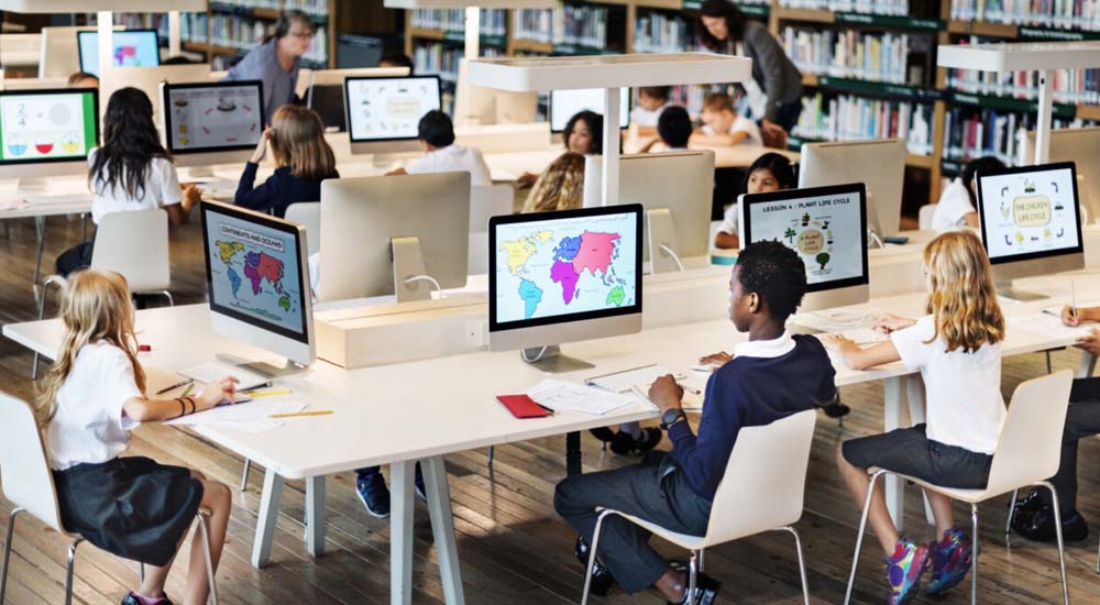 Open kantoorruimte met kinderen achter computers, werkend aan data of geografische software.