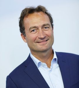 Man met kort bruin haar in blauw net pak met lichte blouse voor lichte achtergrond