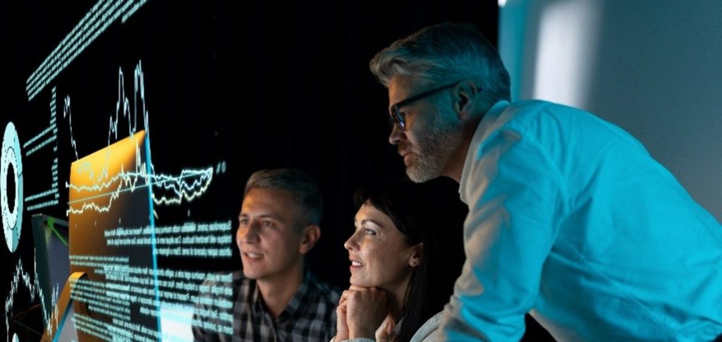 Drie mensen kijken geconcentreerd naar een scherm in een donkere ruimte.