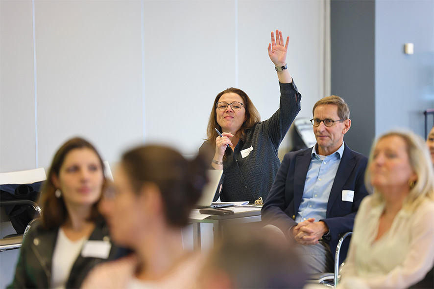 Vrouw steekt haar hand op tijdens een bijeenkomst, omringd door andere deelnemers