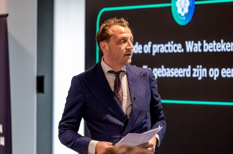 Frans van Bruggen, werkgebiedleider Waarden, Normen en Regelgeving staat voor een scherm en geeft presentatie tijdens een event van AIC4NL.