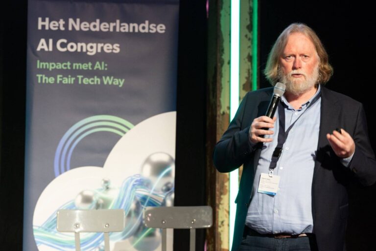 Edwin Kuiper voor een banner met daarop de tekst Het Nederlandse AI Congres - Impact met AI de Fair Tech way, met microfoon in zijn hand.